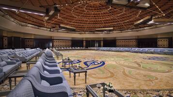 Une salle de conférence spacieuse, dotée de rangées de sièges, d’un tapis à motifs et d’un plafond haut agrémenté de luminaires.