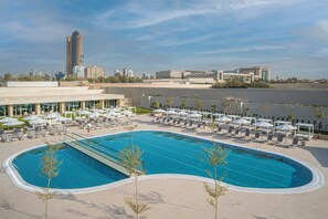 A swimming pool with lounge chairs and umbrellas, a city skyline in the background, and a clear sky.