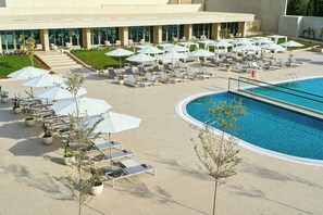 A poolside area with lounge chairs and umbrellas, a swimming pool, and a building with large windows in the background.