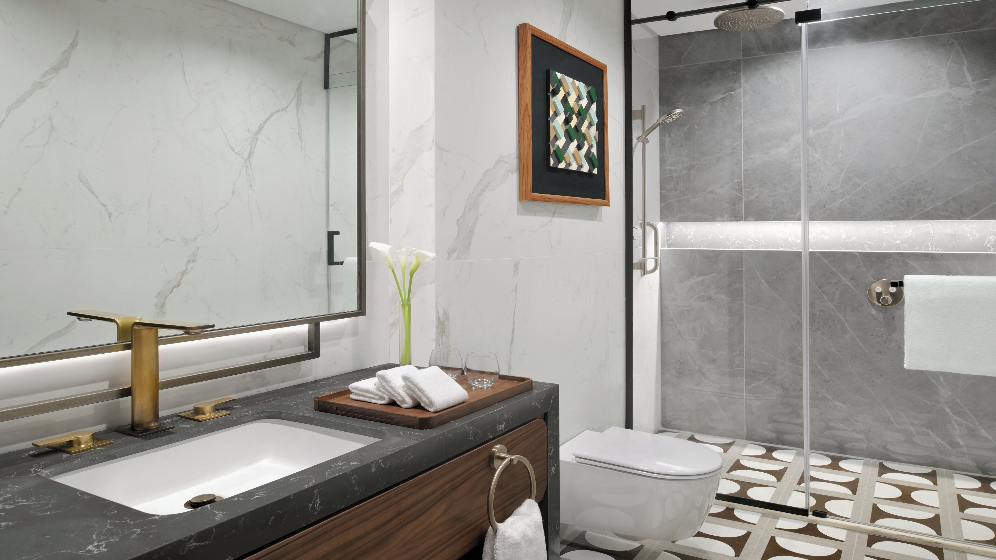 A modern bathroom with a marble sink, a glass shower enclosure, and a toilet with a patterned floor.