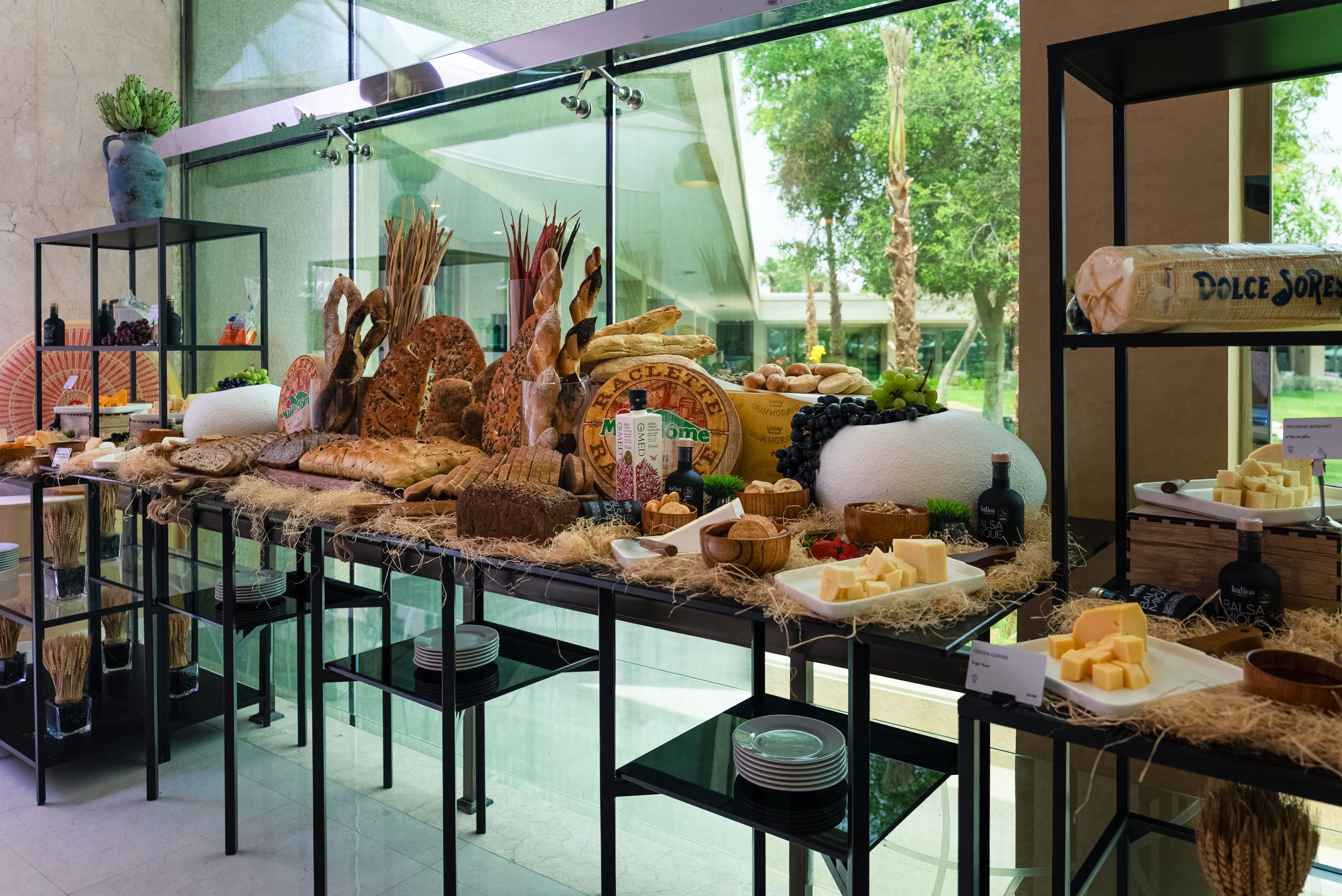 Una mesa de buffet con varios quesos, panes y una botella de vinagre balsámico.