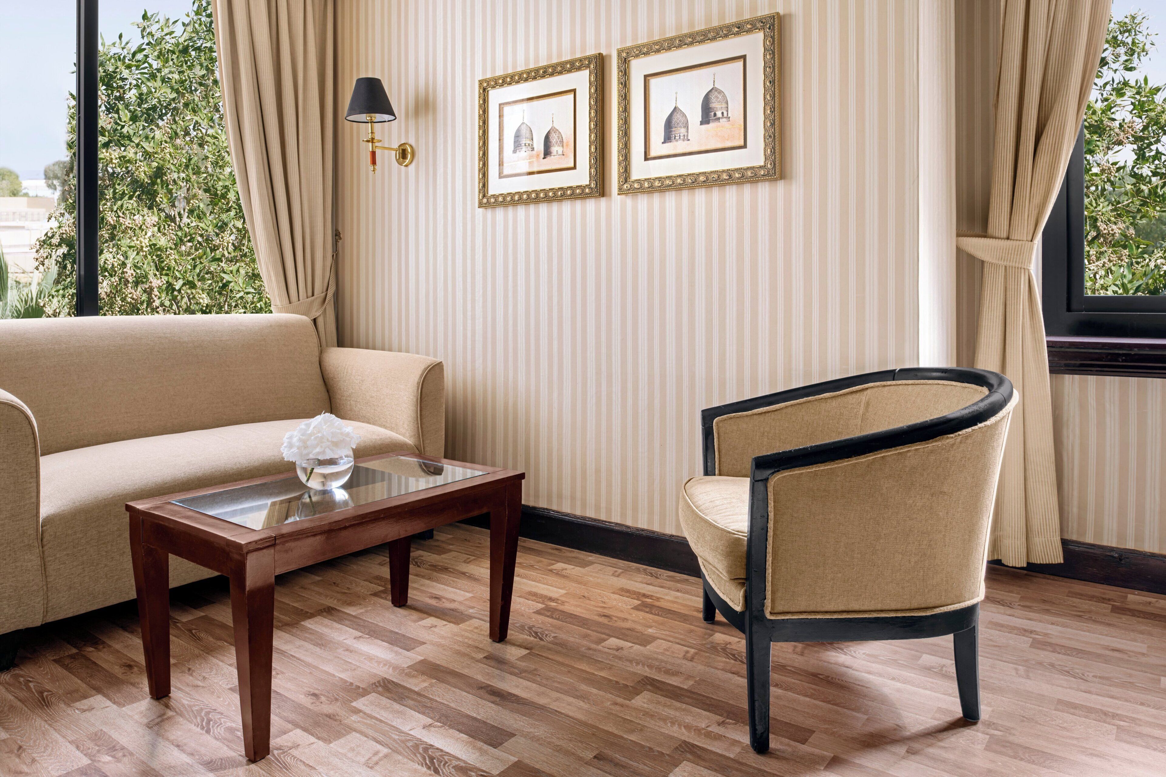 Ein Zimmer mit einer Couch, einem Sessel, einem Glastisch und zwei gerahmten Bildern an der Wand.