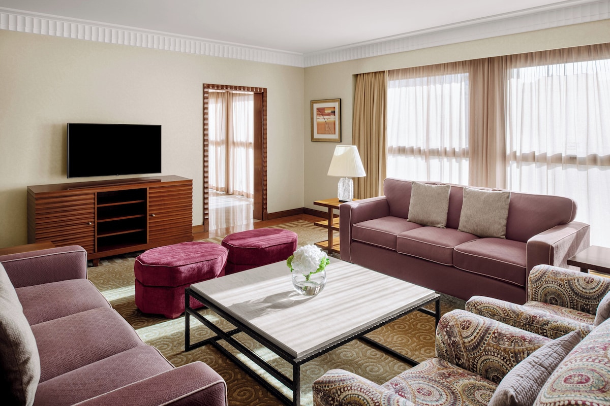 Una sala moderna con una televisión de pantalla plana, un sofá, dos sillones, una mesa de centro y una mesita de noche con una lámpara.