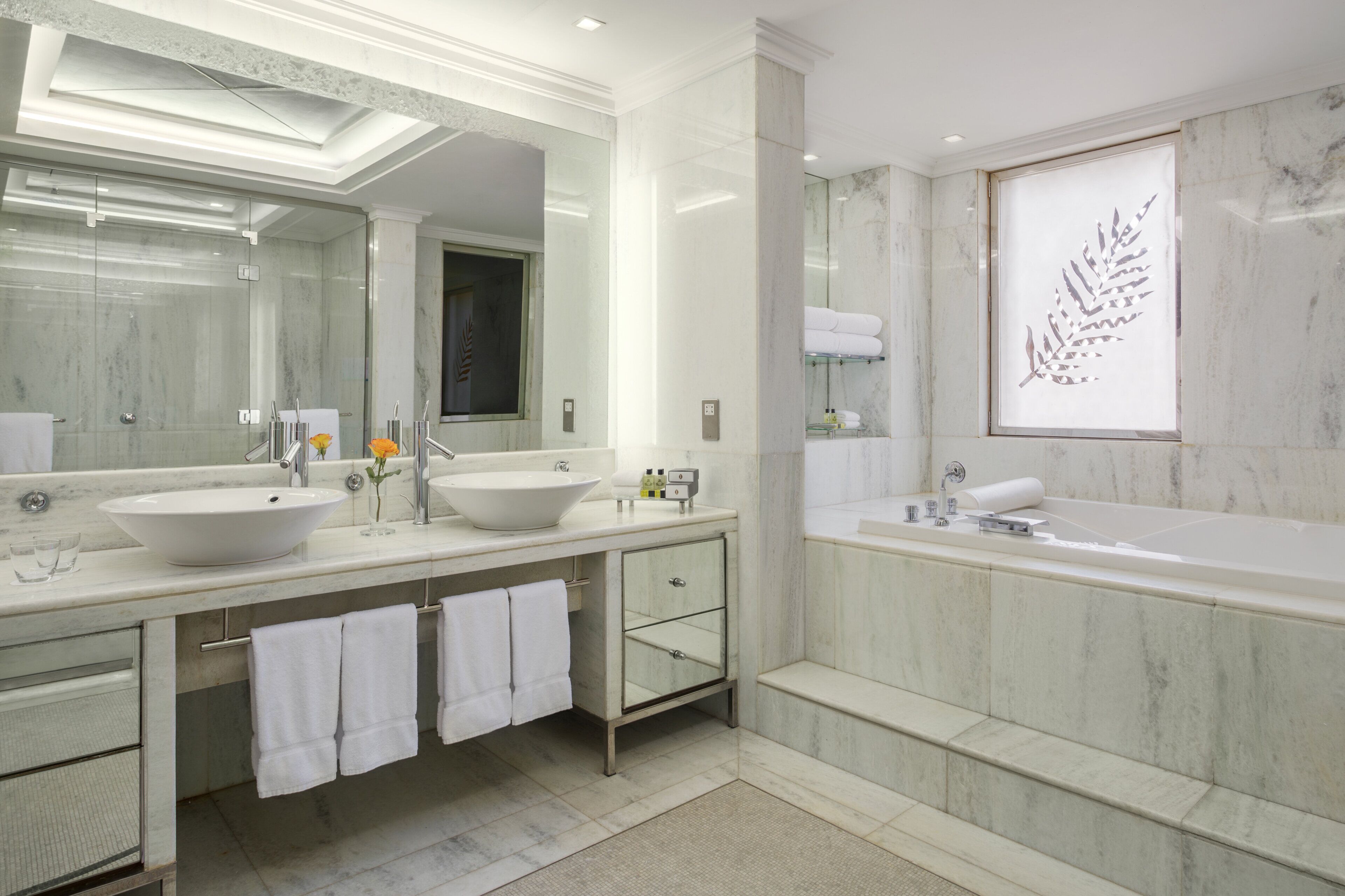 Un baño moderno con dos lavamanos, un espejo grande, una bañera y una obra de arte decorativa con motivos de hojas.