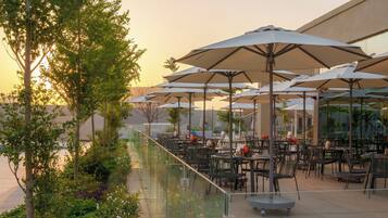 An outdoor patio area with tables and chairs, umbrellas, and a glass railing overlooking a garden.