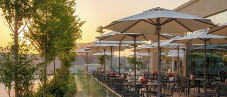 An outdoor patio area with tables and chairs, umbrellas, and a glass railing overlooking a garden.