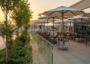An outdoor patio area with tables and chairs, umbrellas, and a glass railing overlooking a garden. - InterContinental Riyadh by IHG (Riyadh)