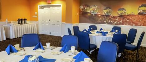 A conference room with round tables, blue chairs, white tablecloths, and a mural on the wall.
