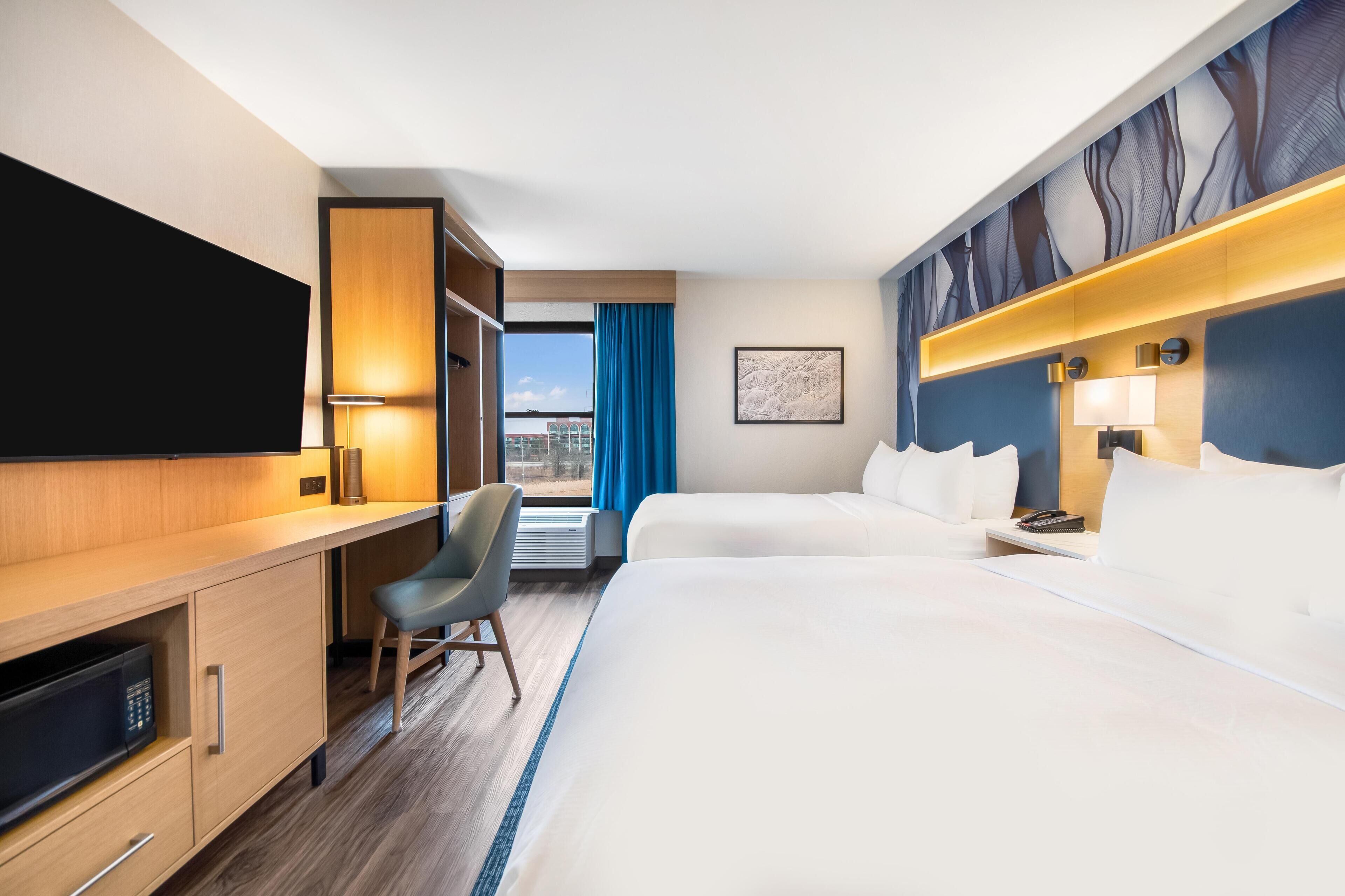 A hotel room with a bed, a desk, a chair, a TV, and a window with curtains.
