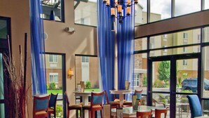 A spacious dining area with wooden tables and chairs, large windows with blue curtains, and a chandelier. - DoubleTree by Hilton Hotel Buffalo - Amherst (Buffalo)
