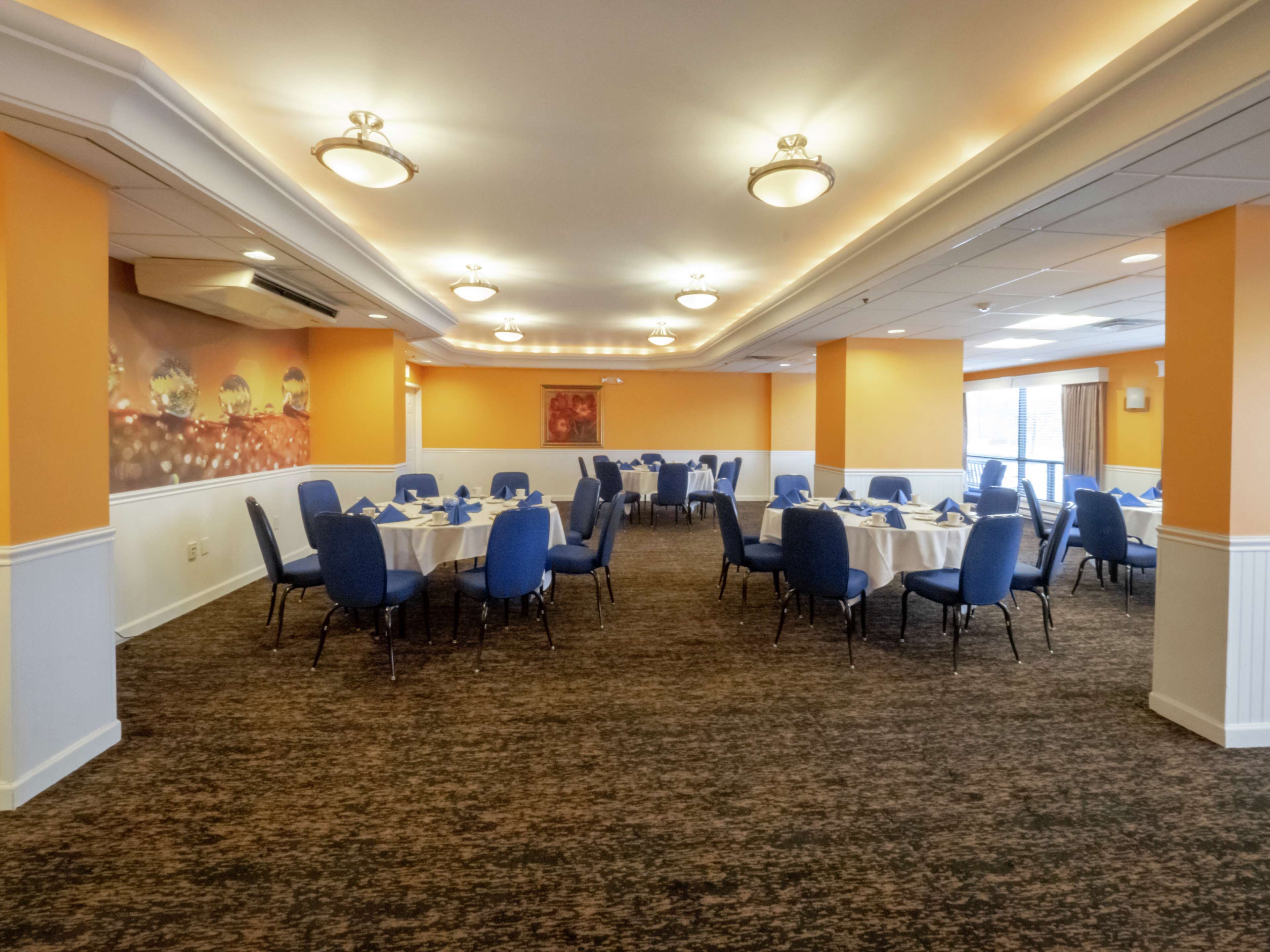 A conference room with multiple tables and chairs, carpeted flooring, and recessed lighting.