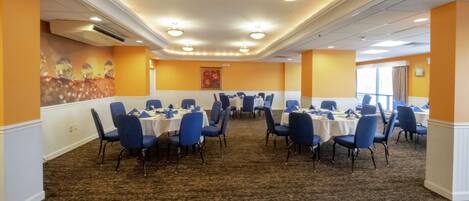 A conference room with multiple tables and chairs, carpeted flooring, and recessed lighting.