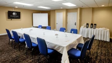 Une salle de conférence avec une longue table, des chaises bleues, un écran de projection et un tableau blanc.