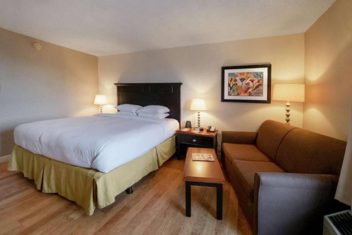Quarto de hotel com cama, sofá, mesa e duas luminárias de cabeceira.