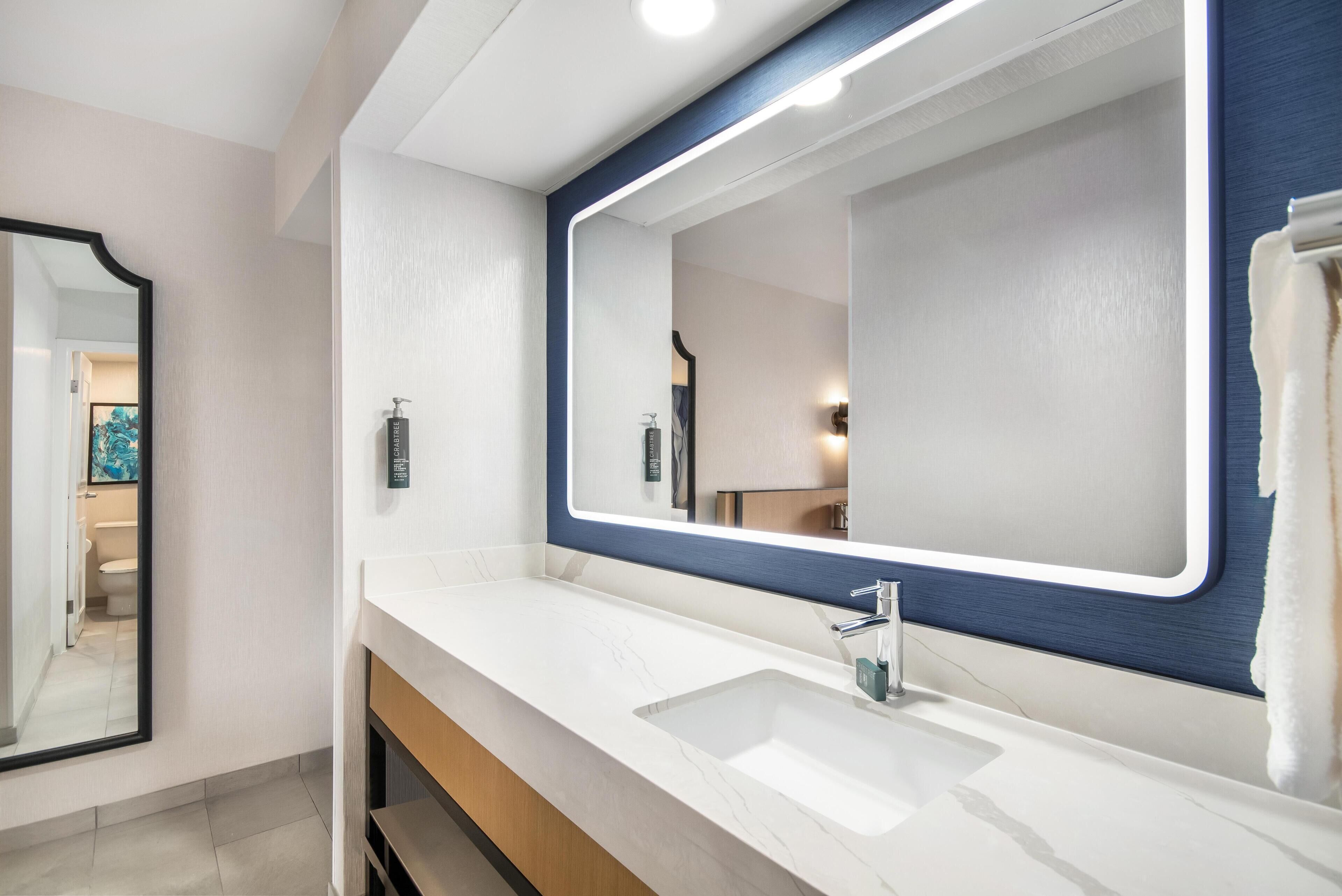 A bathroom with a white sink, a large mirror with a blue frame, and a towel hanging on the wall.