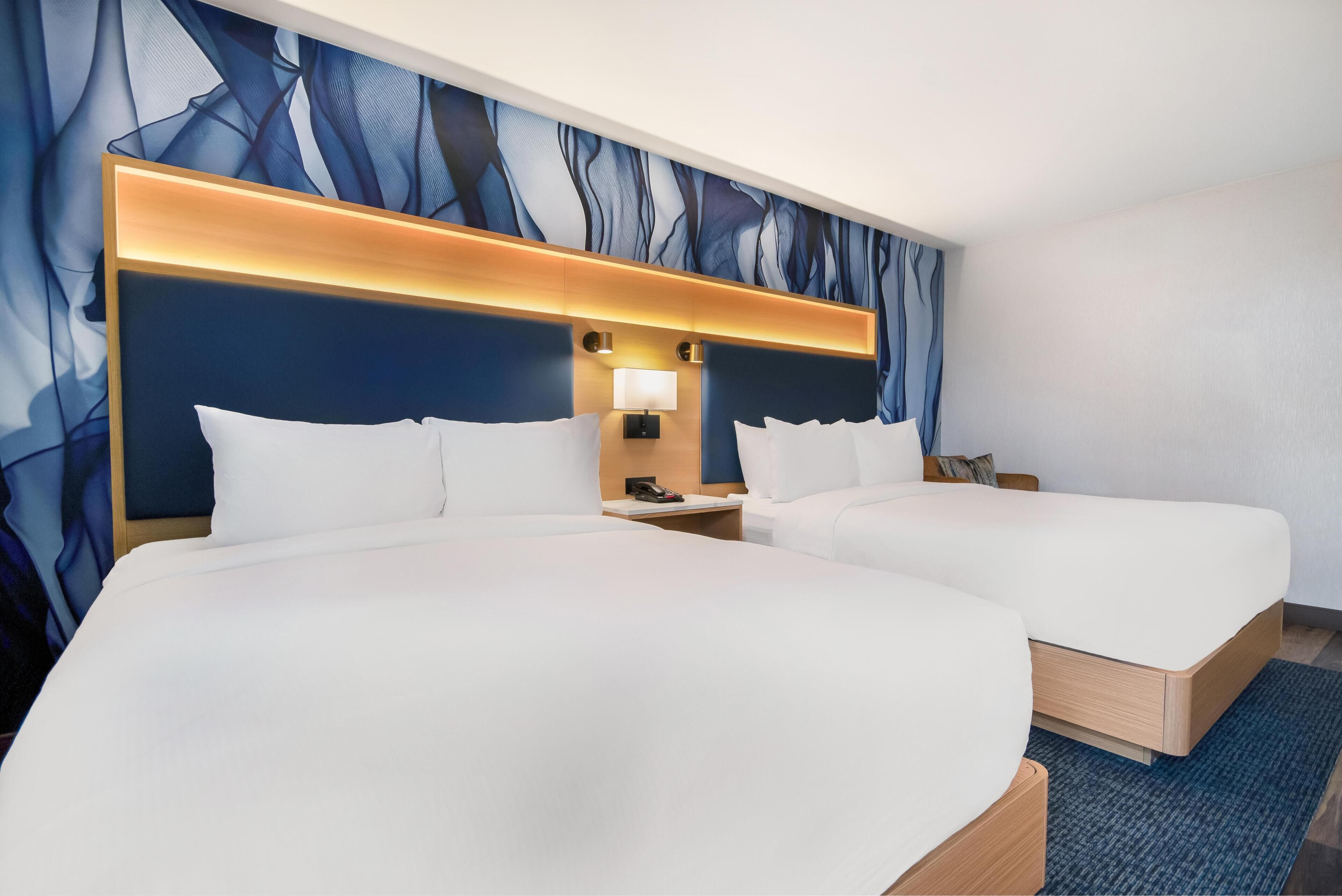 Habitación de hotel con dos camas, un cabecero moderno y un gran mural abstracto en la pared.