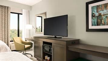 A hotel room with a bed, a desk with a television, a chair, a microwave, and a framed picture on the wall.