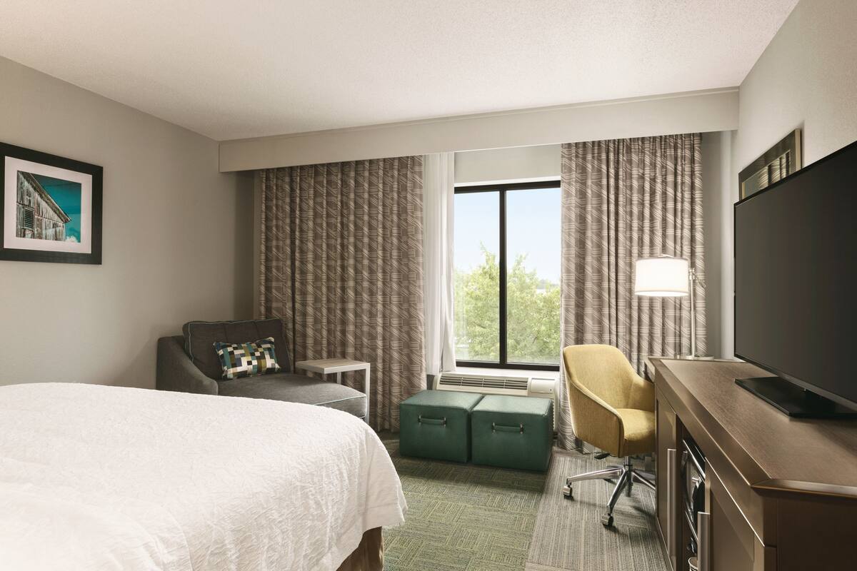 A hotel room with a bed, a desk, a chair, a television, and a window with curtains.