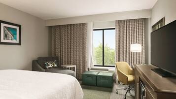 Habitación de hotel con cama, escritorio, silla, televisor y ventana con cortinas.