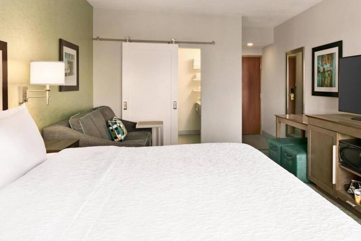 A hotel room with a bed, a desk, a chair, a TV, and a wardrobe.