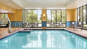 An indoor swimming pool with clear views of trees through large windows, a poolside area with chairs, and a lifeguard stand.