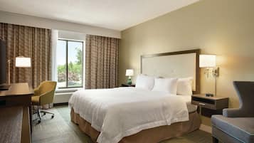 Habitación de hotel con una cama grande, un escritorio, una silla y una ventana con cortinas.