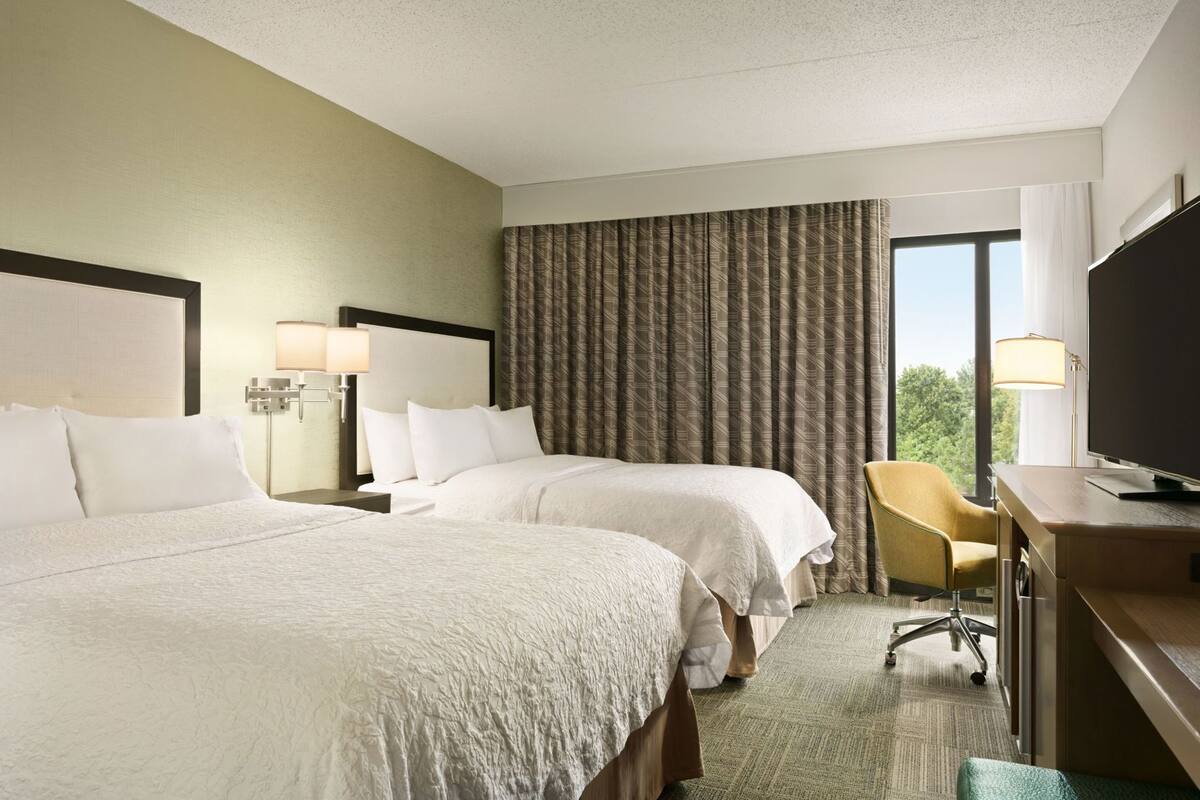 A hotel room with two beds, a desk, a chair, and a television.
