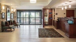 A lobby with a stone wall, two armchairs, a reception desk, a minibar, and a large glass door leading outside.