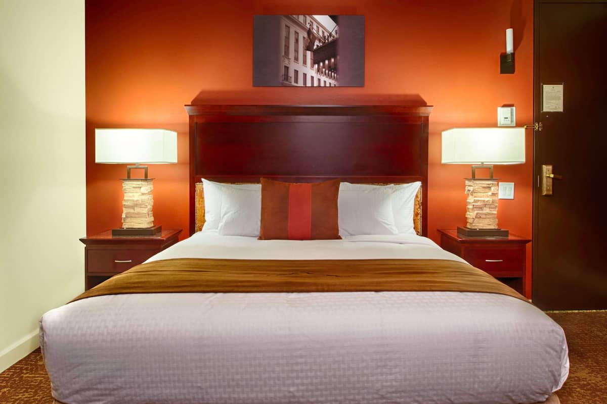 A hotel room with a large bed, two bedside tables with lamps, a wooden headboard, and a framed picture on the wall.