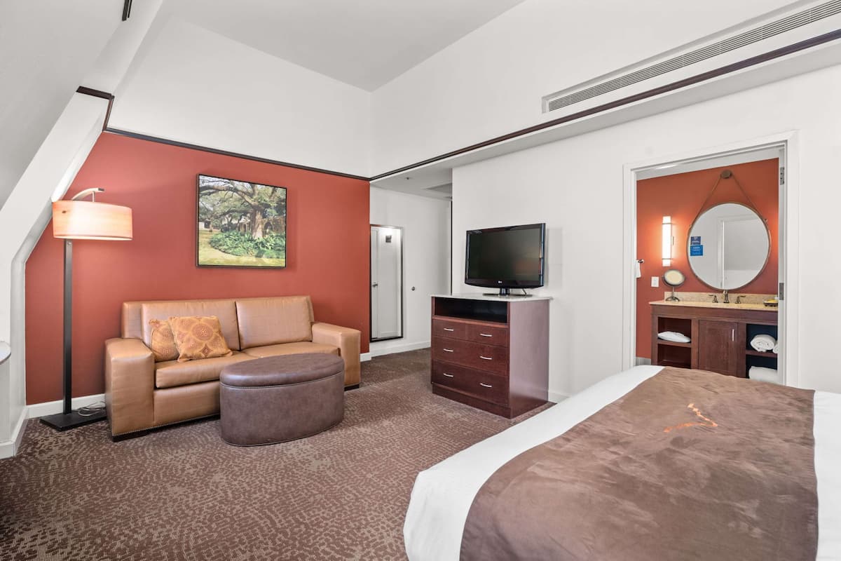 A hotel room with a sofa, ottoman, TV, dresser, and a bed.