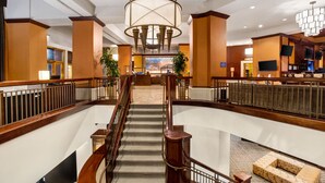 Un vestíbulo de hotel con una escalera monumental, un candelabro y una recepción.