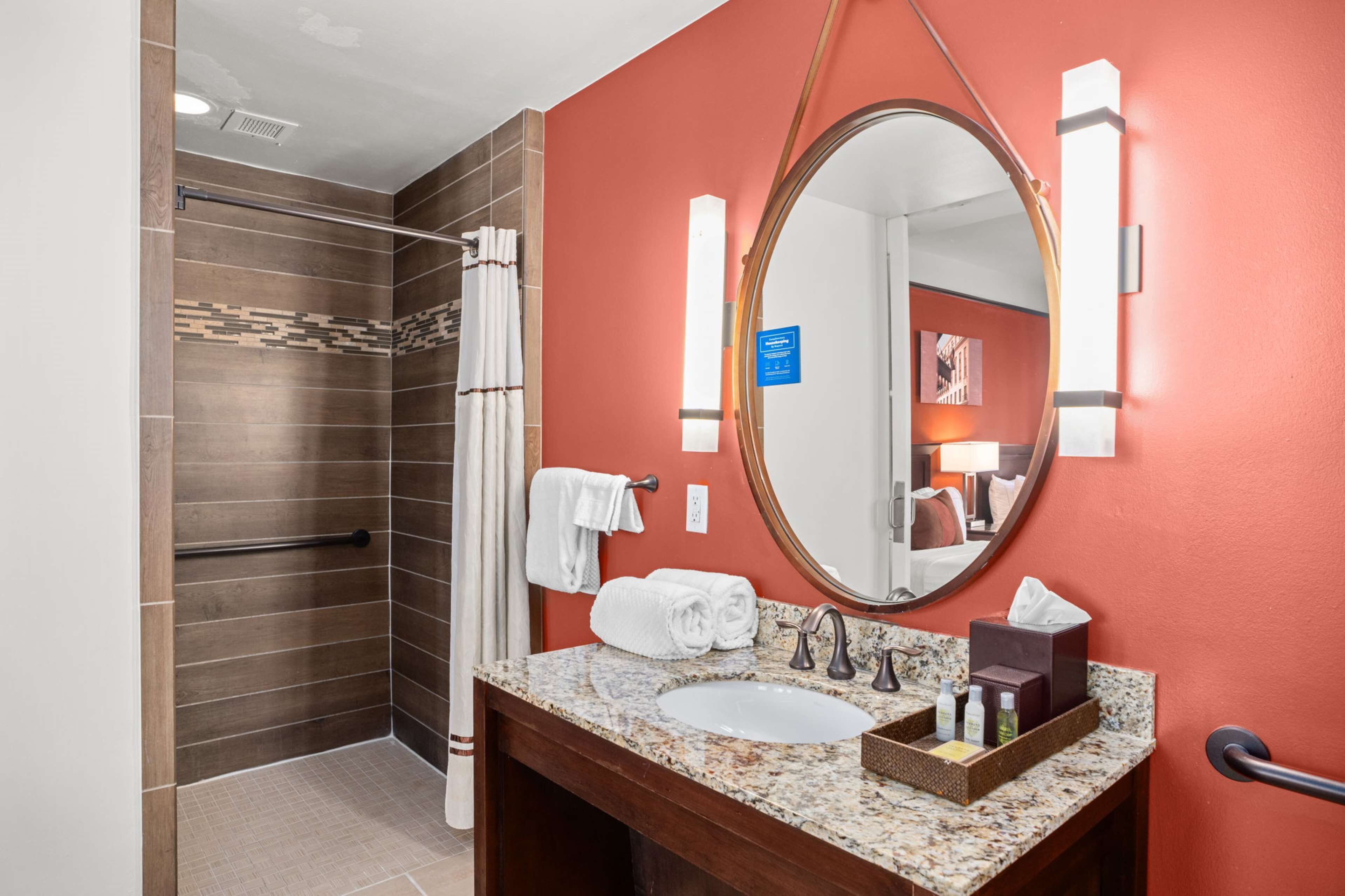 A bathroom with a shower, a sink with a marble countertop, a mirror, and a towel rack.