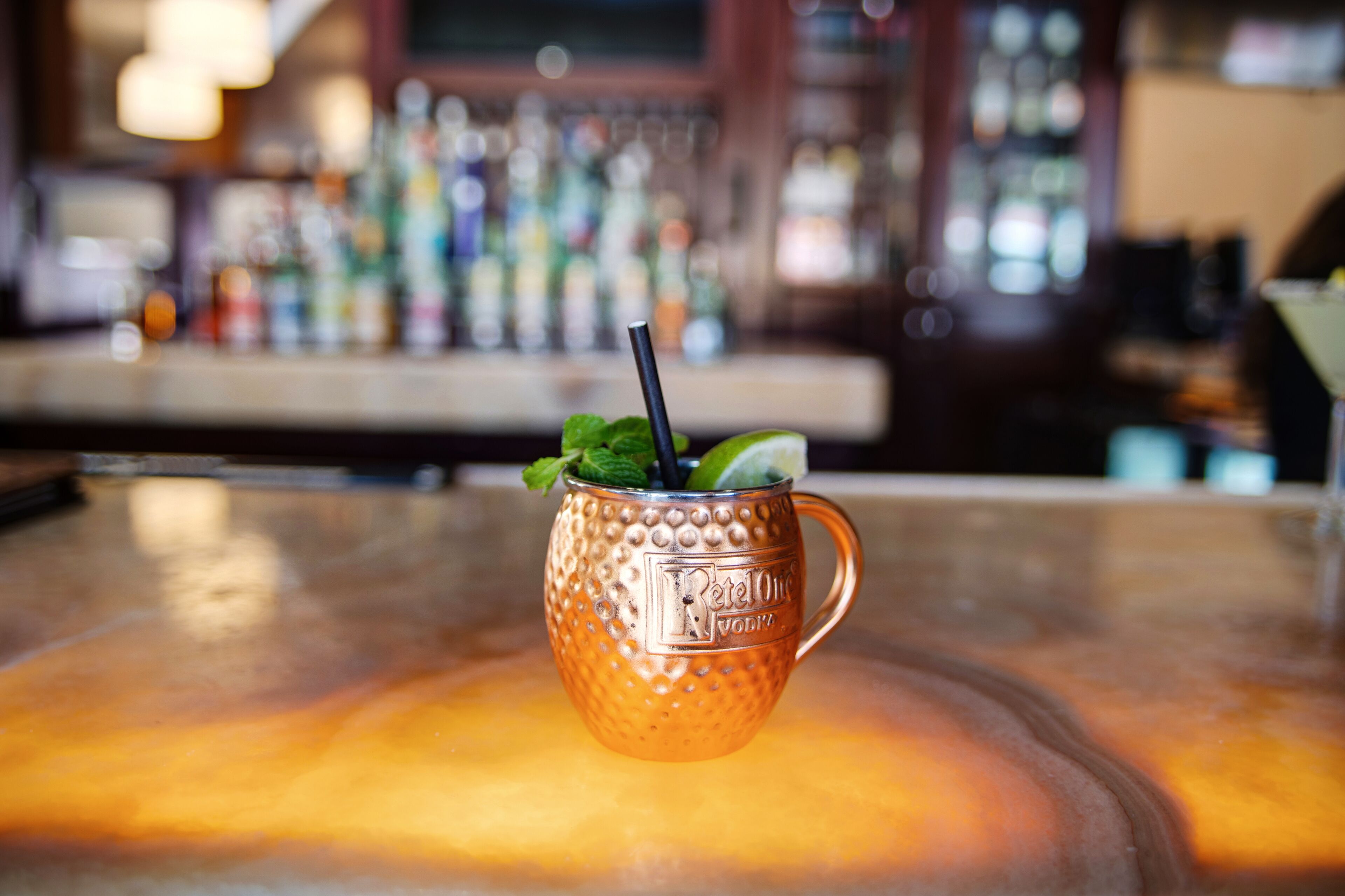 A copper mug with a black straw and mint leaves on a bar counter.