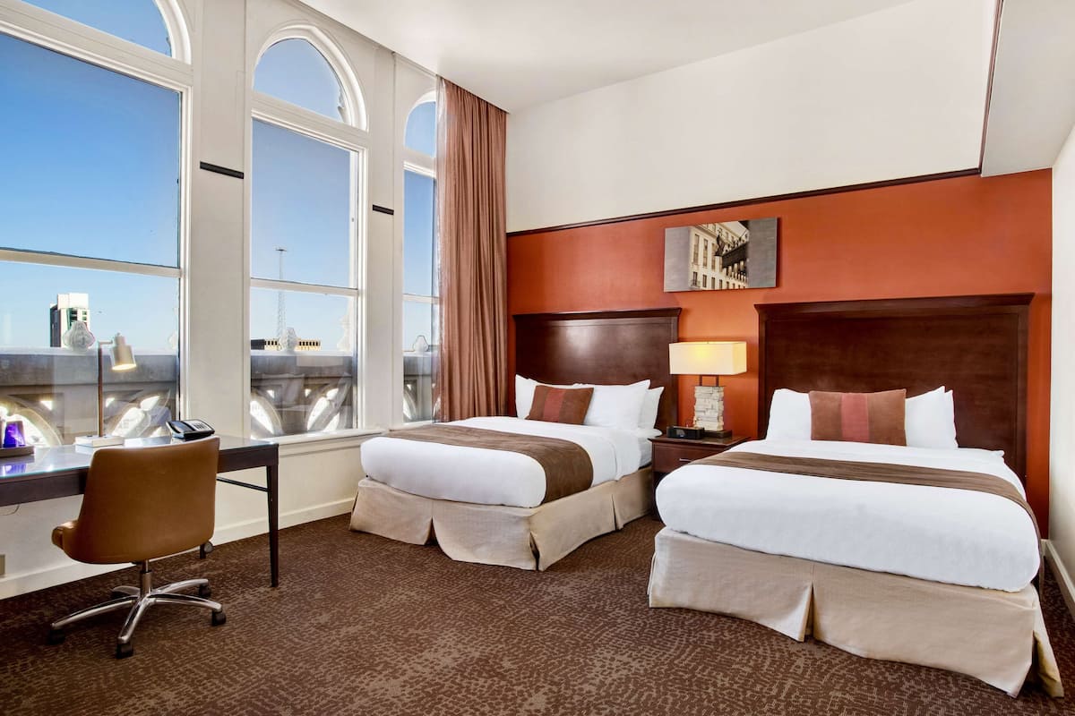 A hotel room with two beds, a desk, and a chair.