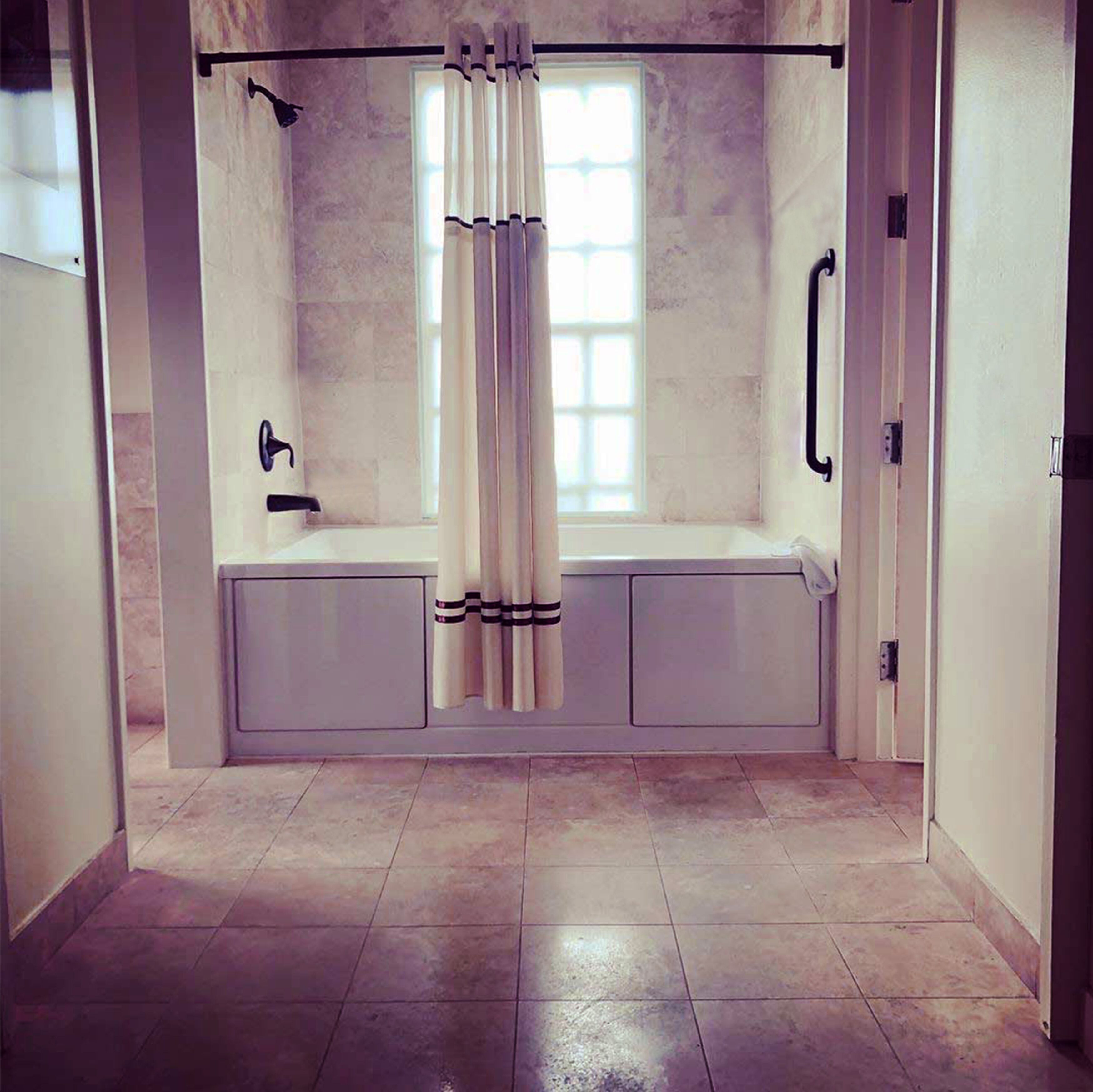Un baño con bañera, ducha y ventana con cortinas.