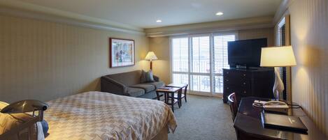 A hotel room with a bed, a desk, a television, a lamp, and a window with blinds.