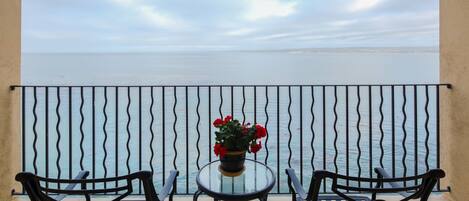 Een balkon met twee stoelen en een tafel, met uitzicht op een rustige zee.