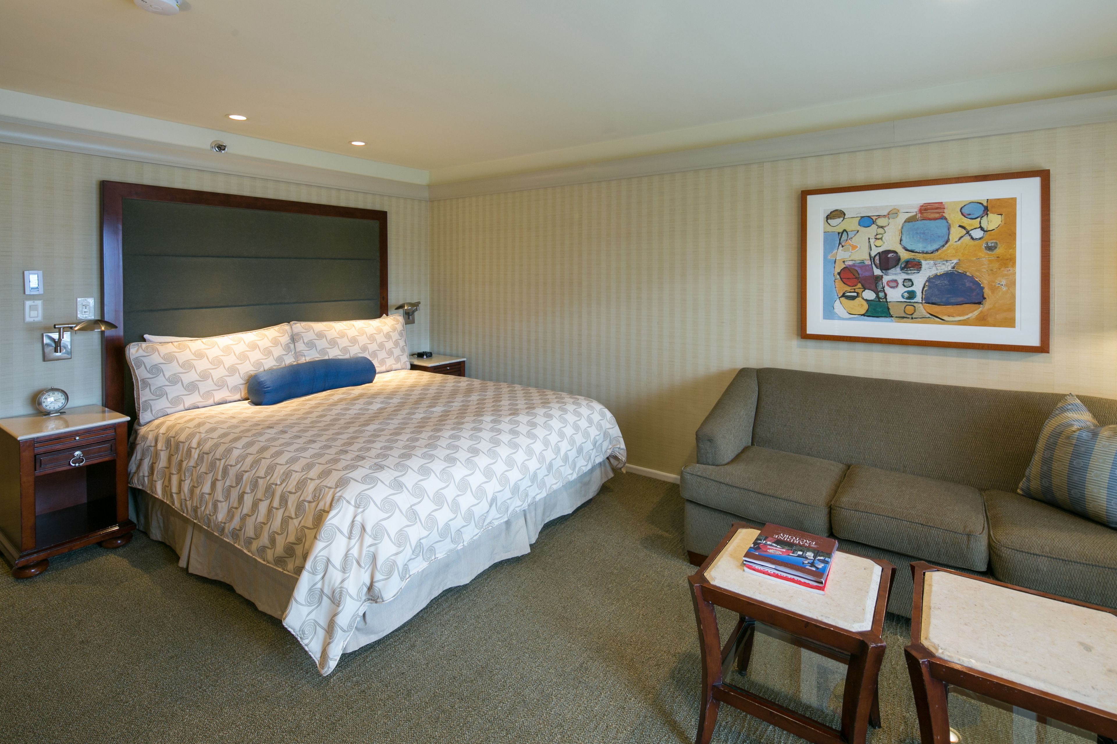 A hotel room with a bed, a sofa, a small table, and a painting on the wall.