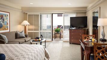A hotel room with a bed, a sofa, a dining table with chairs, a TV, and a balcony with a table and chairs.