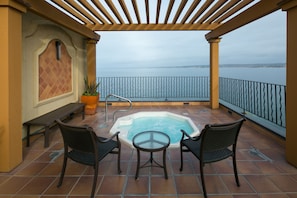 A covered outdoor area with a hot tub, two chairs, a bench, and a potted plant.