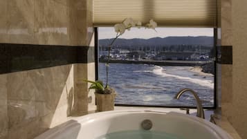 Een badkamer met een bad, een raam met uitzicht op zee en een potorkidee.