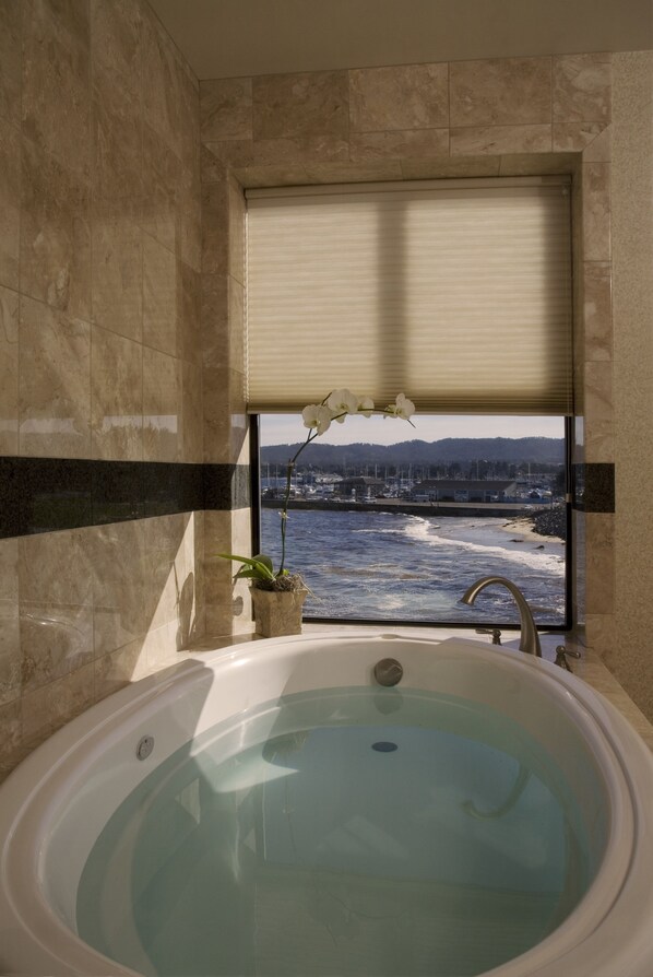 A bathroom with a bathtub, a window with a view of the sea, and a potted orchid.