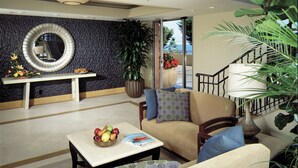 A modern living room with a round mirror, a dining table with fruit, a sofa, and a staircase with a railing. - Monterey Bay Inn (Monterey)
