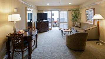 A hotel room with a dining table, a sofa, a TV, and a balcony with a view.