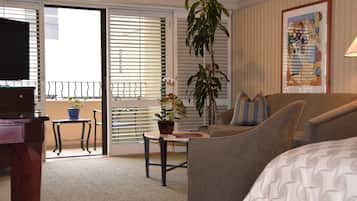 A hotel room with a sofa, a small table with a plant, a TV, and a balcony with a railing.