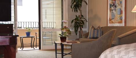 Habitación de hotel con sofá, una pequeña mesa con planta, televisor y balcón con barandilla.