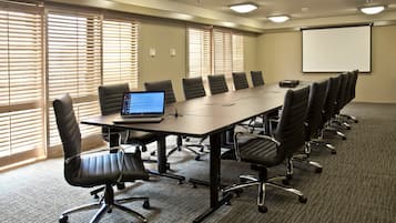 A conference room with a long table, multiple chairs, a laptop, and a projector screen.
