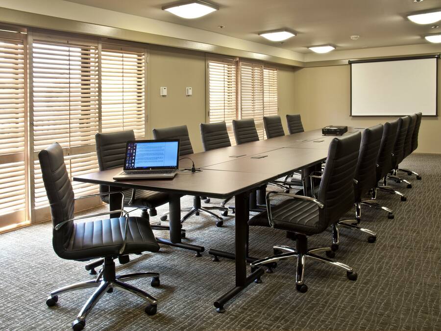 A conference room with a long table, multiple chairs, a laptop, and a projector screen.