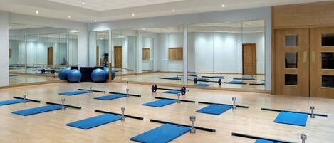 Un gimnasio amplio con paredes de espejo, colchonetas de ejercicio y equipamiento.