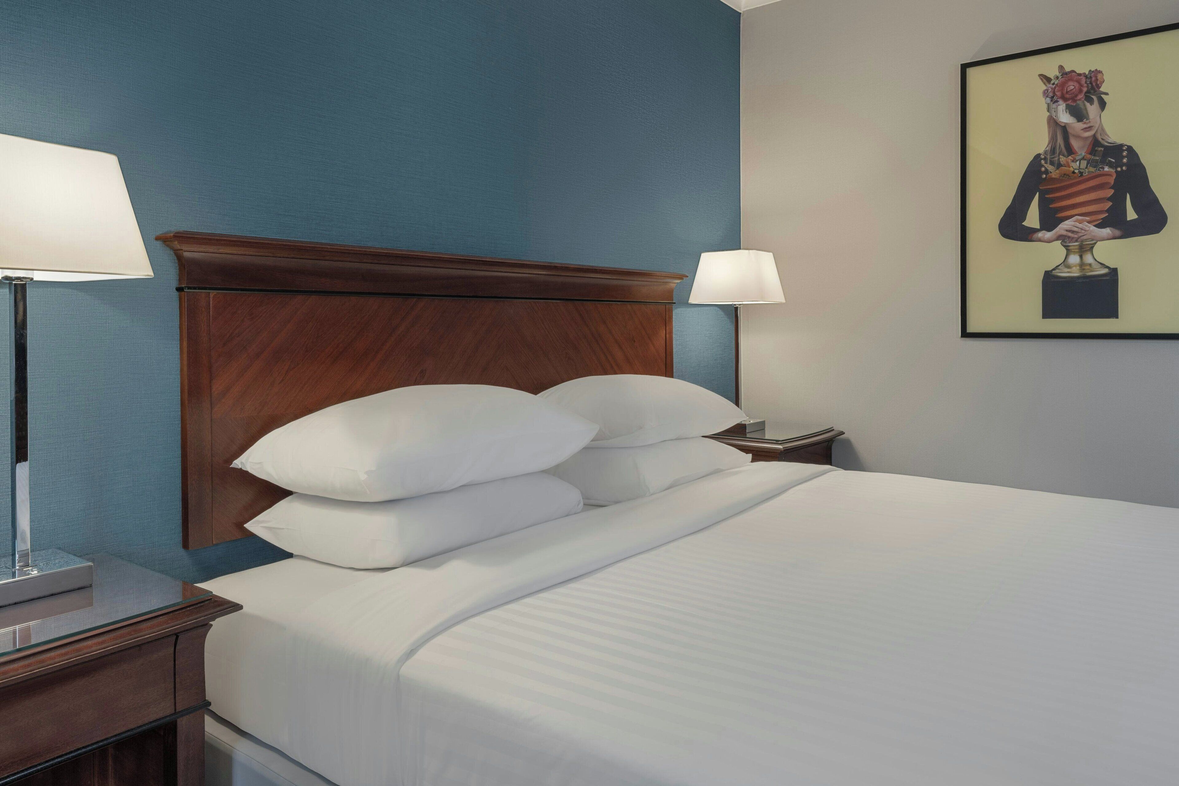 Habitación de hotel con cabecera de madera, ropa de cama blanca y una obra de arte enmarcada en la pared.